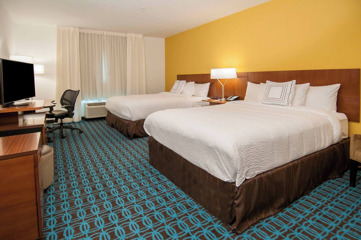 A hotel room with two beds, a desk with a computer, and a chair.