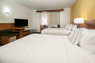 A hotel room with two beds, a TV, a desk, and a lamp.