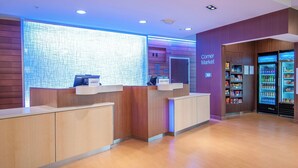 A hotel reception area with a wooden reception desk, a digital screen, and a 'Corner Market' sign. - Fairfield Inn & Suites by Marriott LaPlace (LaPlace)
