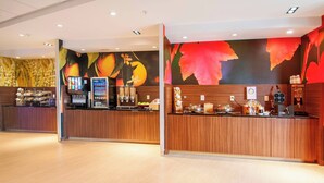 A modern hotel reception area with a wooden counter, a vending machine, and a wall with a fruit mural. - Fairfield Inn & Suites by Marriott LaPlace (LaPlace)