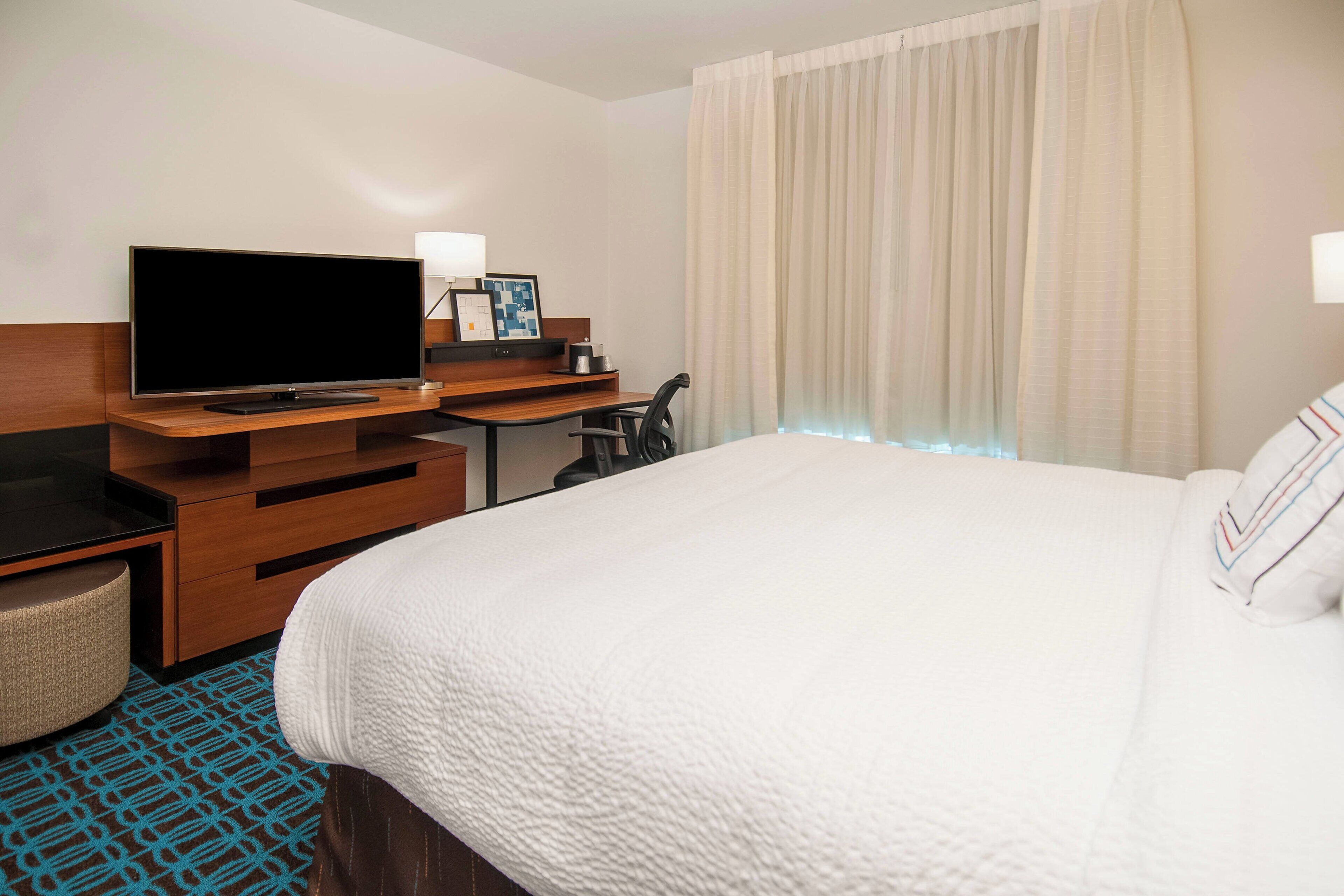 A hotel room with a bed, a desk with a flat-screen TV, a chair, and a small seating area.