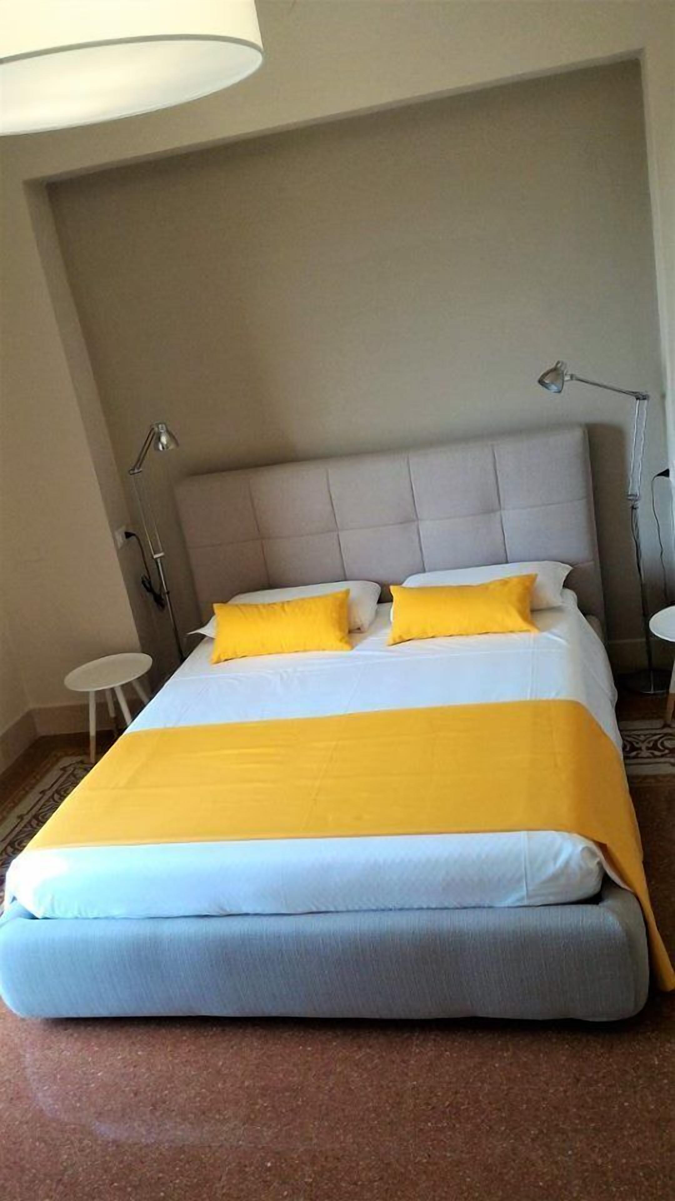 Una habitación de hotel con una cama grande, dos lámparas de noche, una mesita redonda y un ventanal amplio.