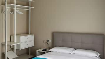 A hotel room with a bed, a white bedside table, a lamp, a wardrobe, and a patterned floor.