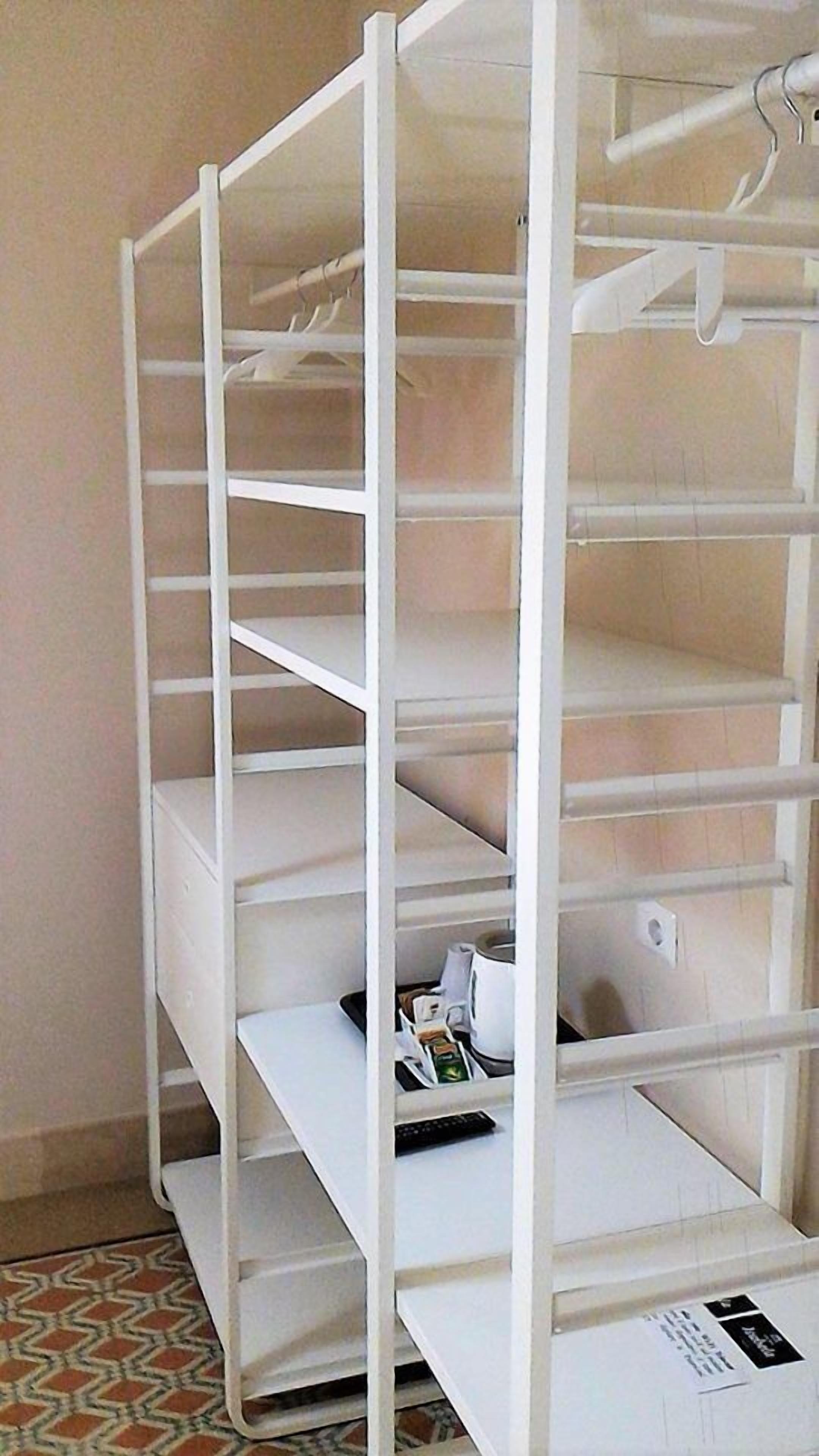 A white metal shelving unit with multiple shelves, some containing items like a remote control and a kettle.