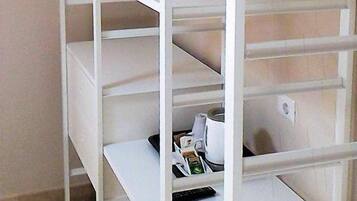 A white metal shelving unit with multiple shelves, some containing items like a remote control and a kettle.