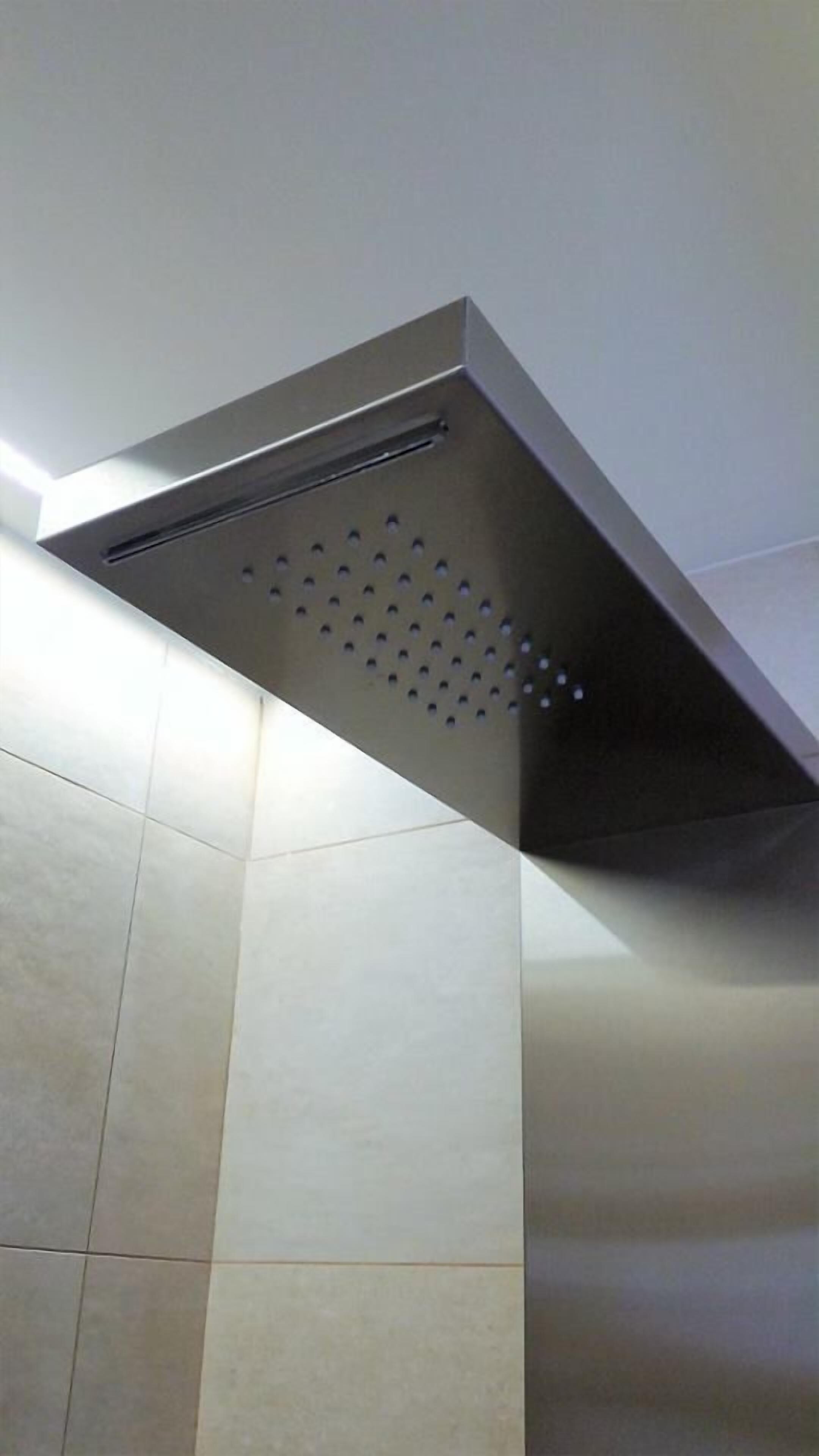 A modern shower with a sleek, metallic design and a perforated panel for water flow.