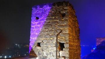 A stone tower with a partially illuminated facade, featuring a visible entrance and several small openings.