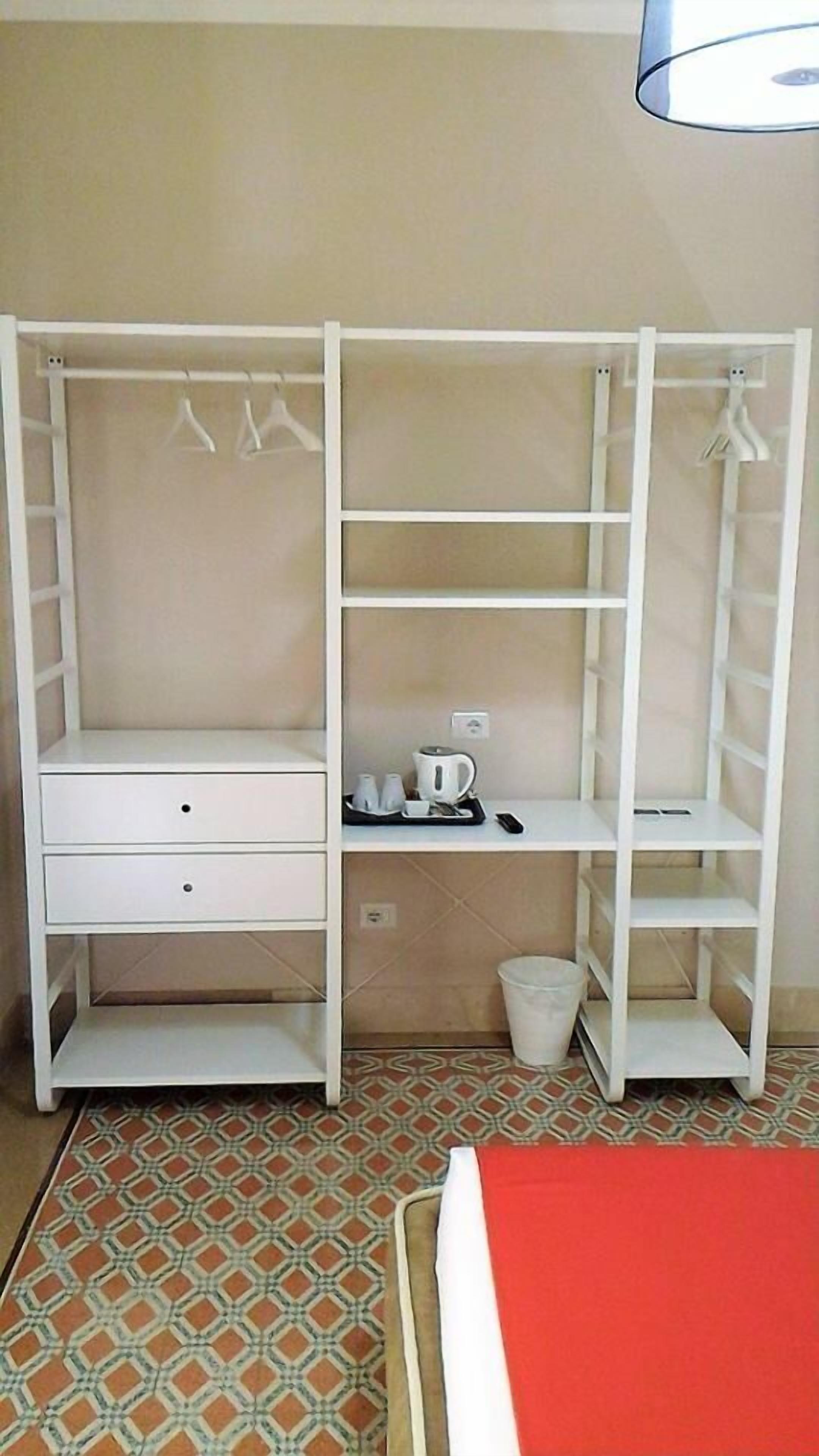 Ein Zimmer mit einem weißen Kleiderschrank, einem kleinen Schreibtisch und einem roten Bett.