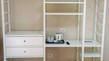 Ein Zimmer mit einem weißen Kleiderschrank, einem kleinen Schreibtisch und einem roten Bett.