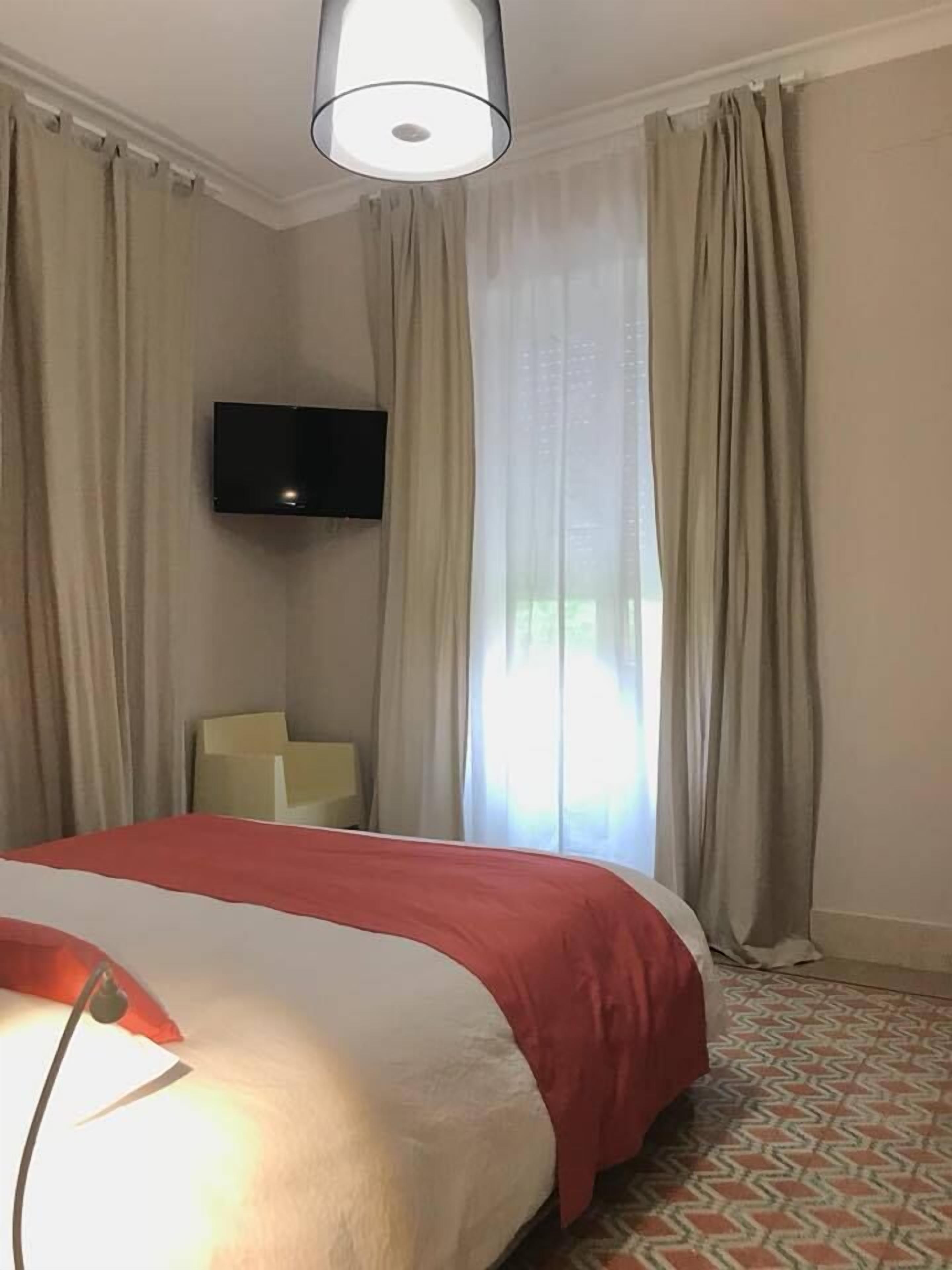 A hotel room with a bed, a TV mounted on the wall, and a chair.