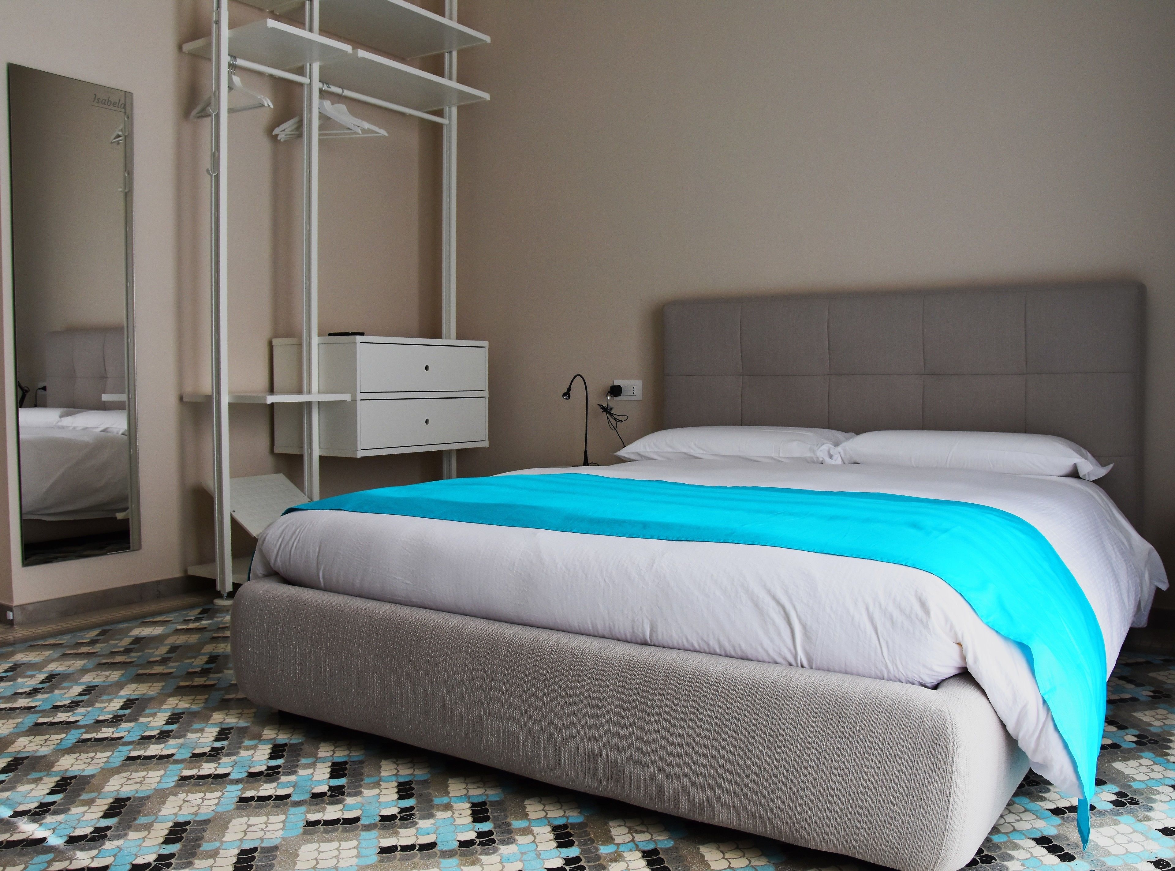 A neatly arranged bedroom with a bed, a bedside table, a wardrobe, and a mirror.