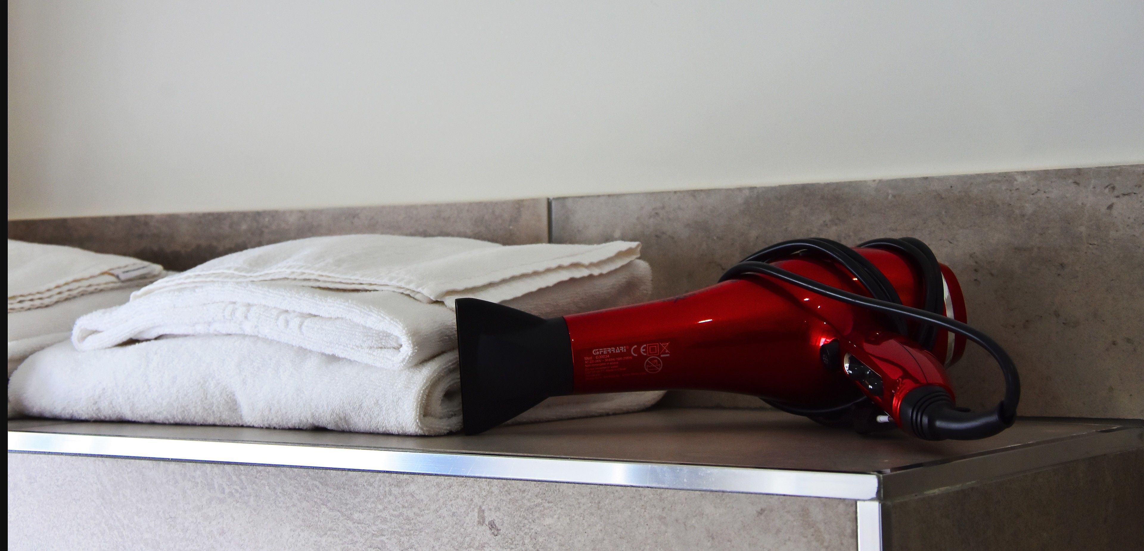 A red hair dryer on a bathroom counter next to folded towels.