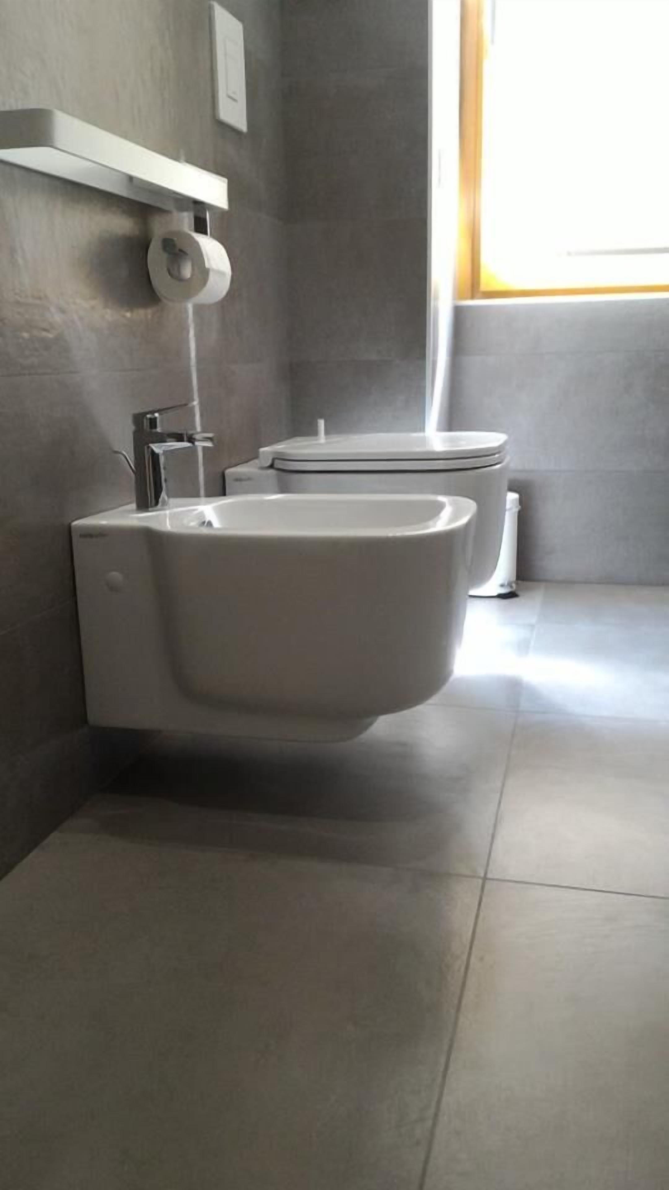 A modern bathroom with a bidet, a toilet, and a shelf with a roll of toilet paper.