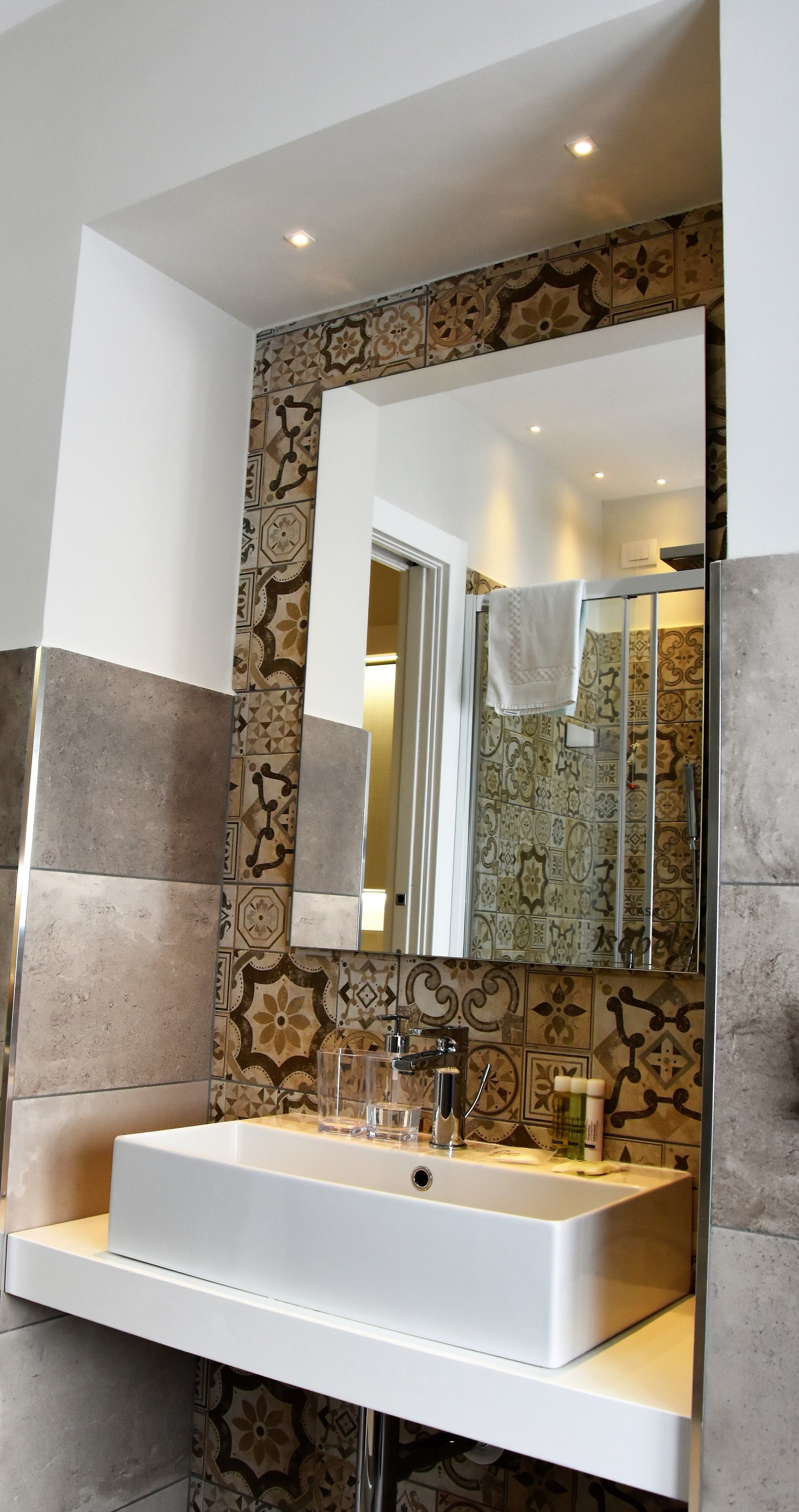 Un baño con un espejo grande, un lavamanos blanco y azulejos con diseño en las paredes.