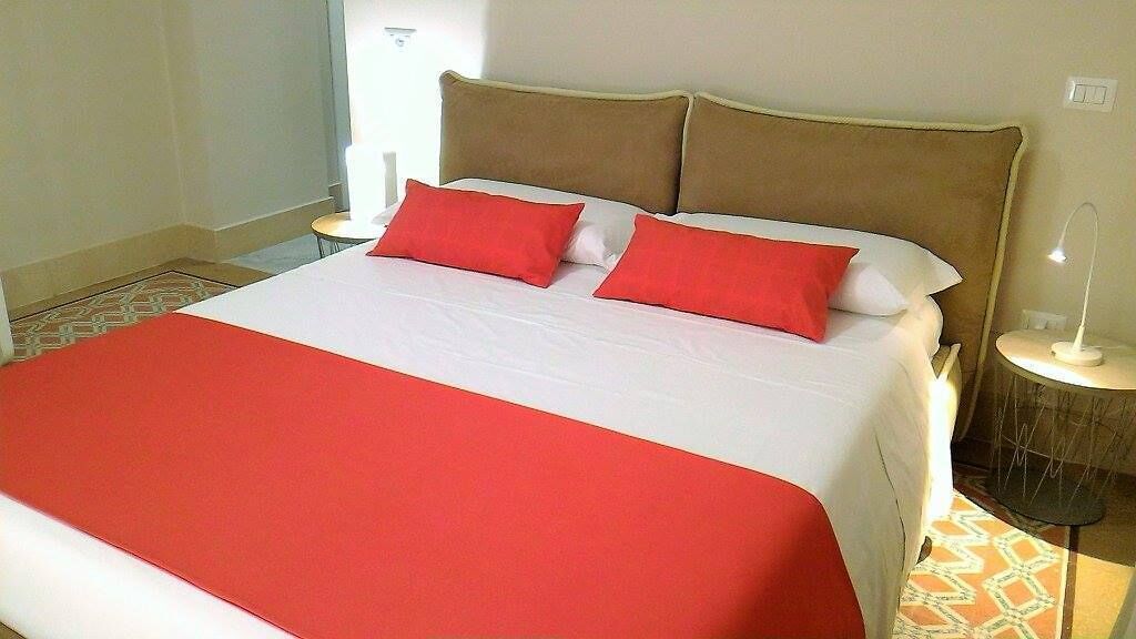 Un lit avec une couvre-lit rouge et blanche, deux oreillers rouges et une tête de lit marron.