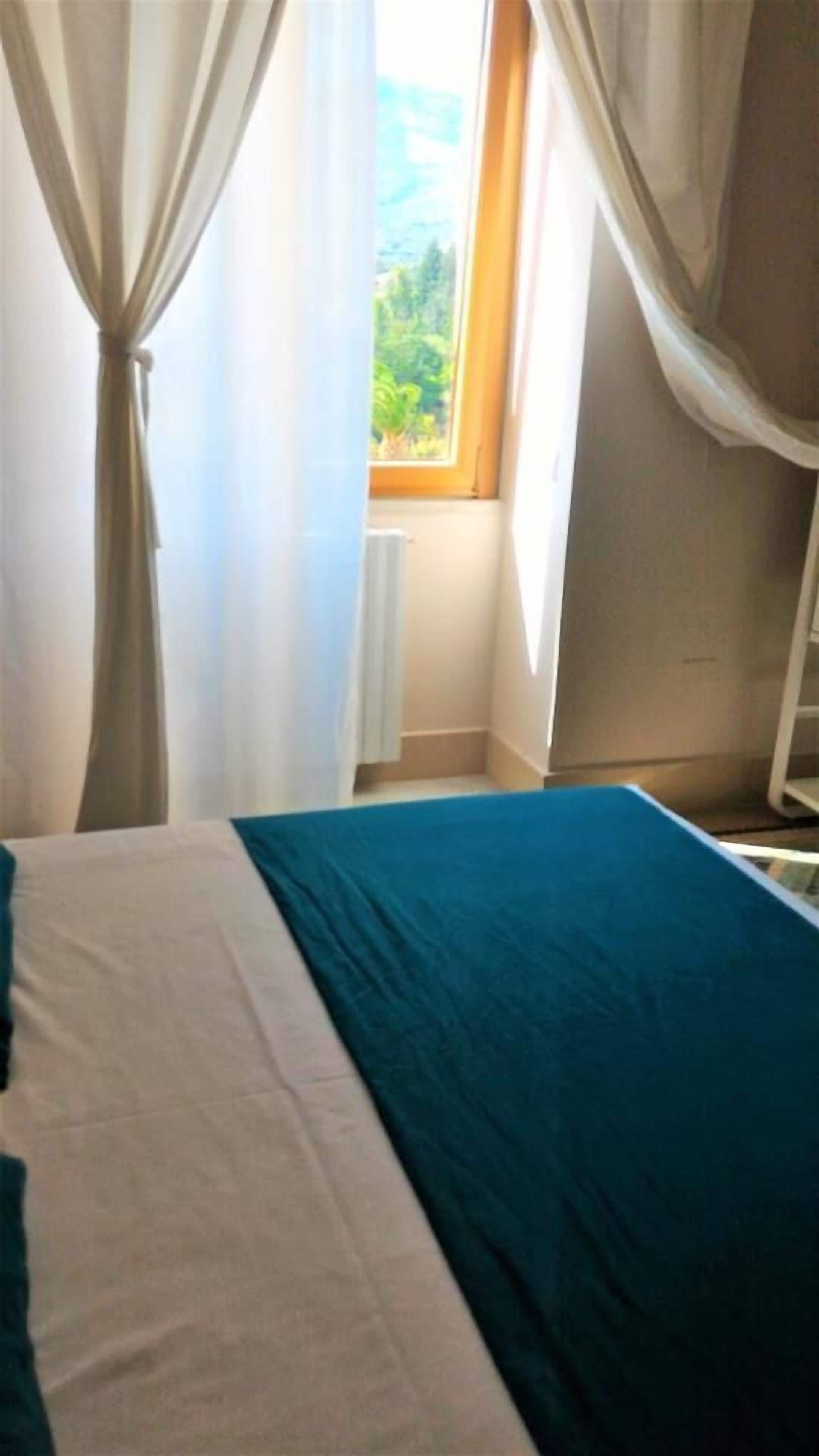 A bedroom with a bed, a window with curtains, and a radiator.