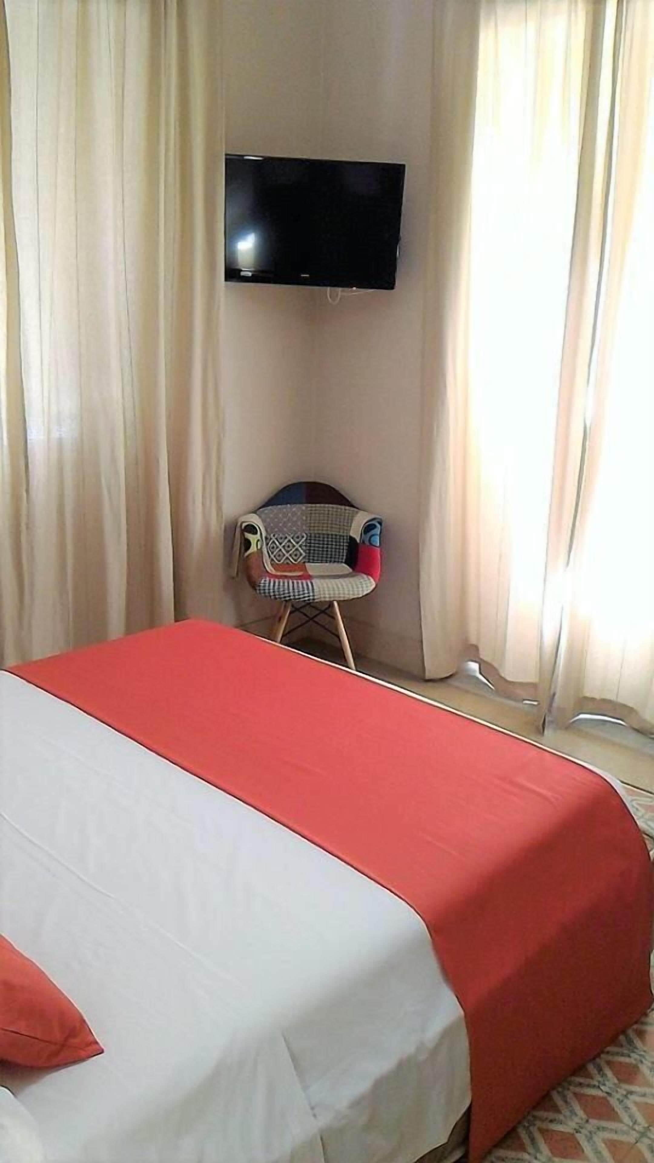 A hotel room with a bed, a TV mounted on the wall, a chair, and curtains.