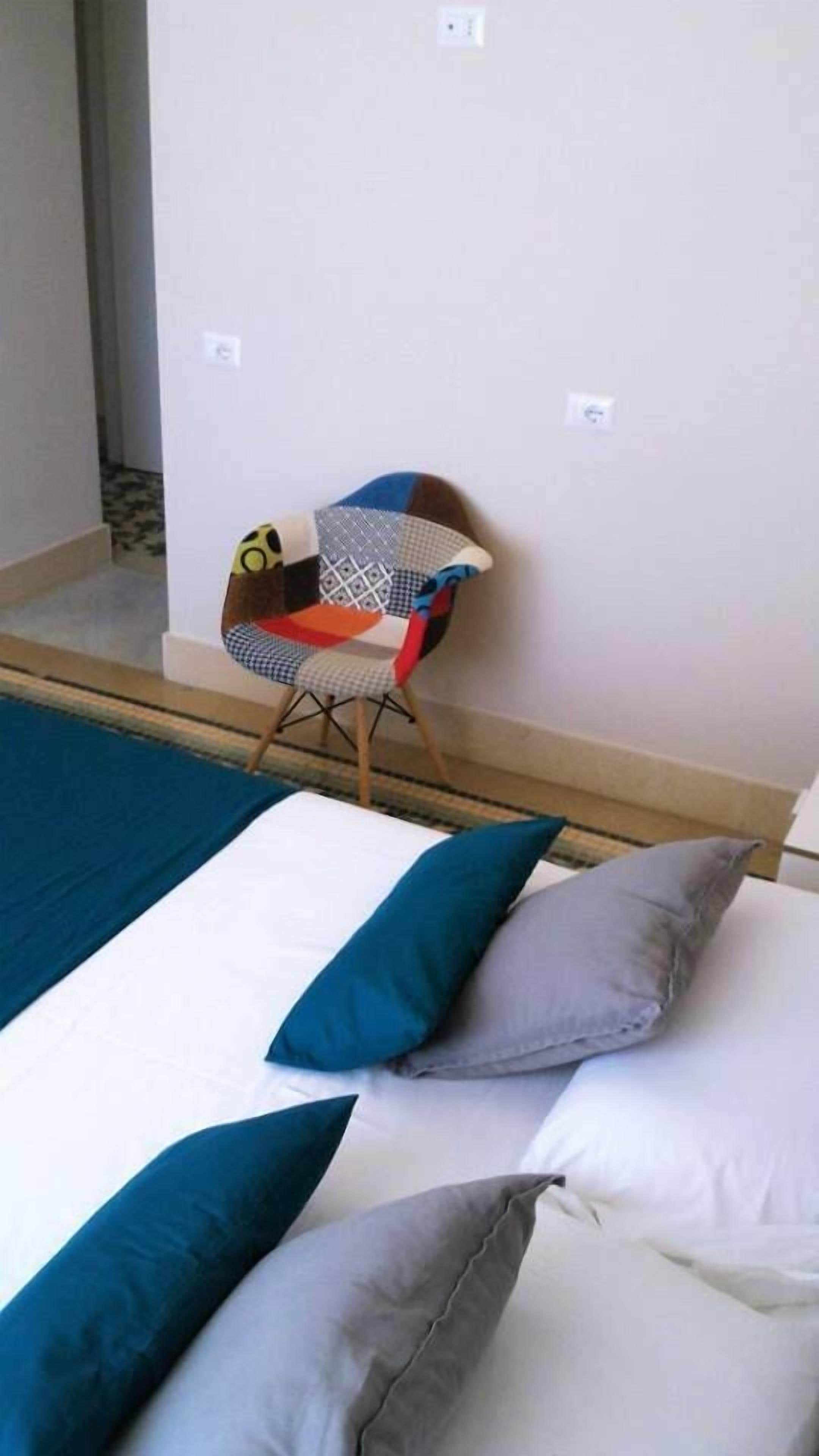Una habitación con cama, almohadas, una silla y un papel tapiz estampado.