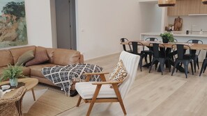A living room with a sofa, a patterned throw, a chair, a dining table with chairs, and a kitchen area. - ADAGIO in the Gold Links estate Point Lonsdale (Point Lonsdale)