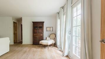 A spacious room with hardwood flooring, a large wooden cabinet, a chair, and a large window with curtains.
