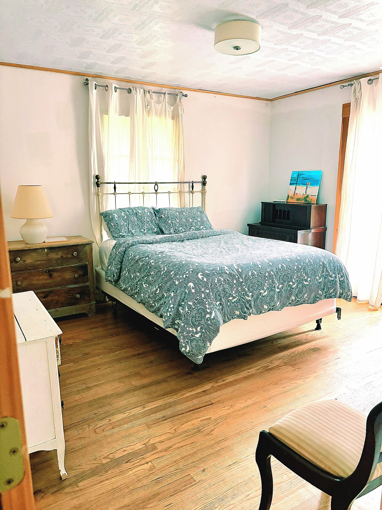 A bedroom with a bed, a nightstand, a dresser, a chair, and a painting on the wall.