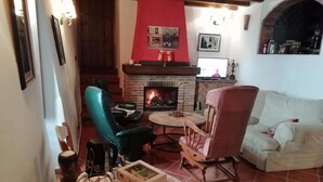 Un salon chaleureux avec une cheminée, des fauteuils en cuir, un canapé blanc et un sol carrelé.