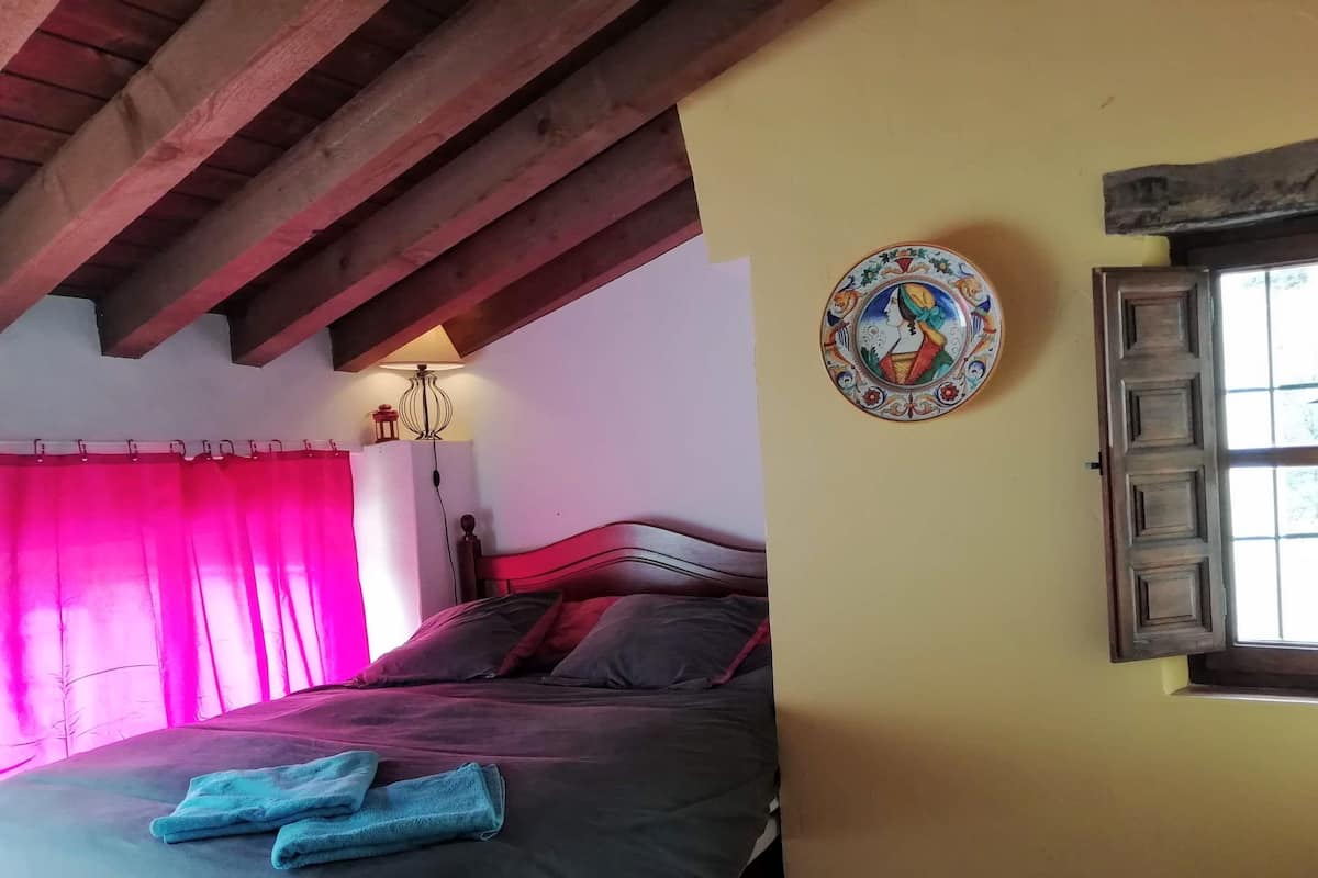 Ein Schlafzimmer mit einem Bett, einer Lampe, einem Fenster mit Fensterläden und einer dekorativen Platte an der Wand.