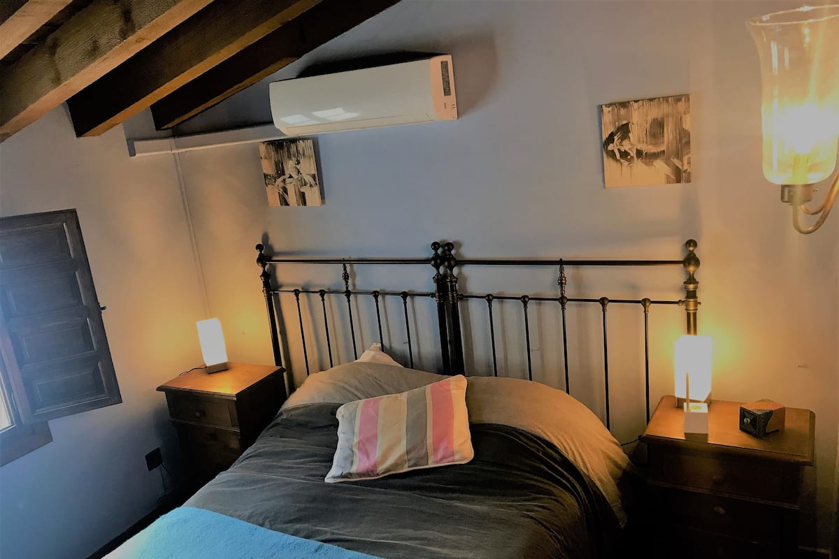 Ein Schlafzimmer mit einem Bett, zwei Nachttischen, einer Klimaanlage und Wandbildern.
