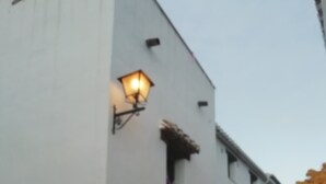 Un bâtiment blanc avec une cour dallée de pierres, un banc en bois et des plantes en pot.