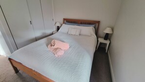 Siististi pedattu sänky, jossa on rullalle taitettu pyyhe, kaksi yöpöytää valaisimineen ja puinen pääty.
