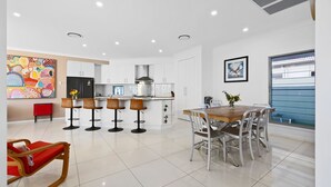 A modern kitchen with white cabinets, a stainless steel range hood, and a bar area with stools. - Splash House at Kingscliff - Pet Friendly with Pool (KINGSCLIFF)