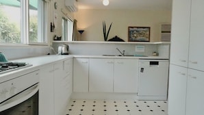 A compact kitchen with white cabinets, a stove, a sink, and a dishwasher.