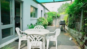 A patio with a table and chairs, a barbecue grill, and a garden area with plants and a fence.