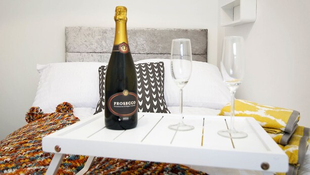 A bed with a white headboard, a bottle of Prosecco, and two glasses on a tray. - Haven Apartments at Eglantine Avenue (Belfast)