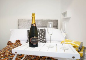 A bed with a white headboard, a bottle of Prosecco, and two glasses on a tray.