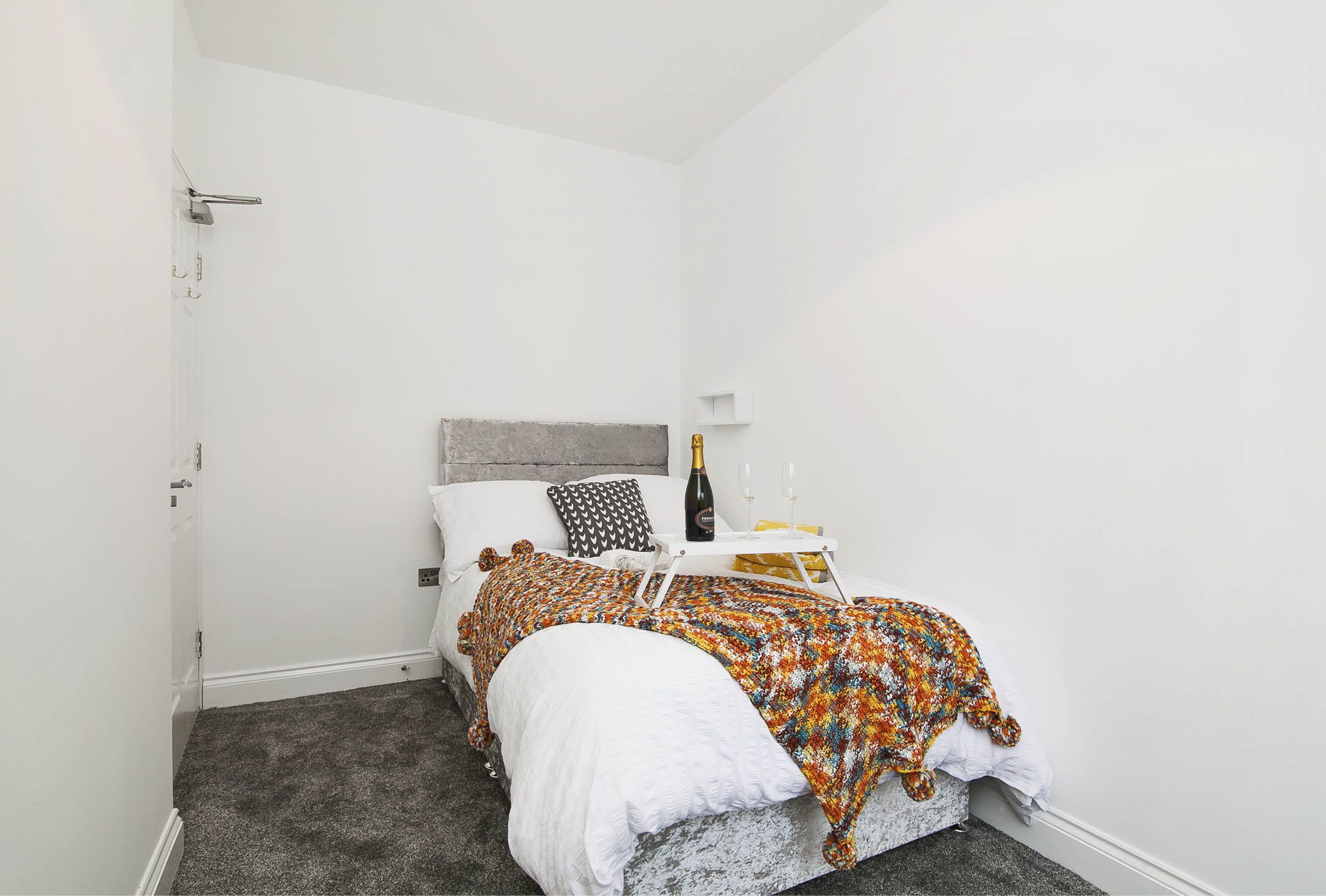 A bedroom with a bed, a nightstand, a bottle of champagne, and a small table with two glasses.