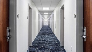 Een lange, smalle hotelgang met deuren aan beide kanten, genummerde bordjes en een kamerbreed tapijt.