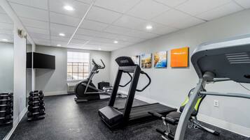 Una palestra con tapis roulant, manubri e uno specchio.