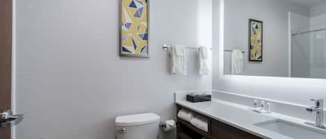 Un baño con inodoro, lavamanos y espejo. Hay toallas colgadas en la pared y un cuadro enmarcado sobre el espejo.