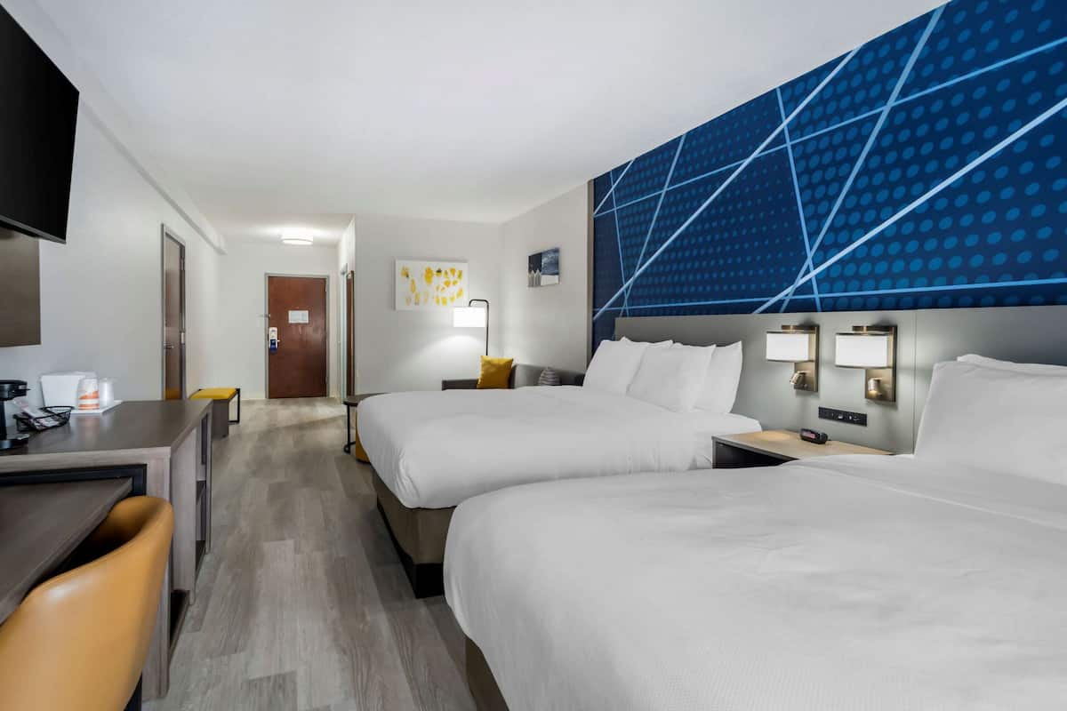 A hotel room with two beds, a desk, and a TV.