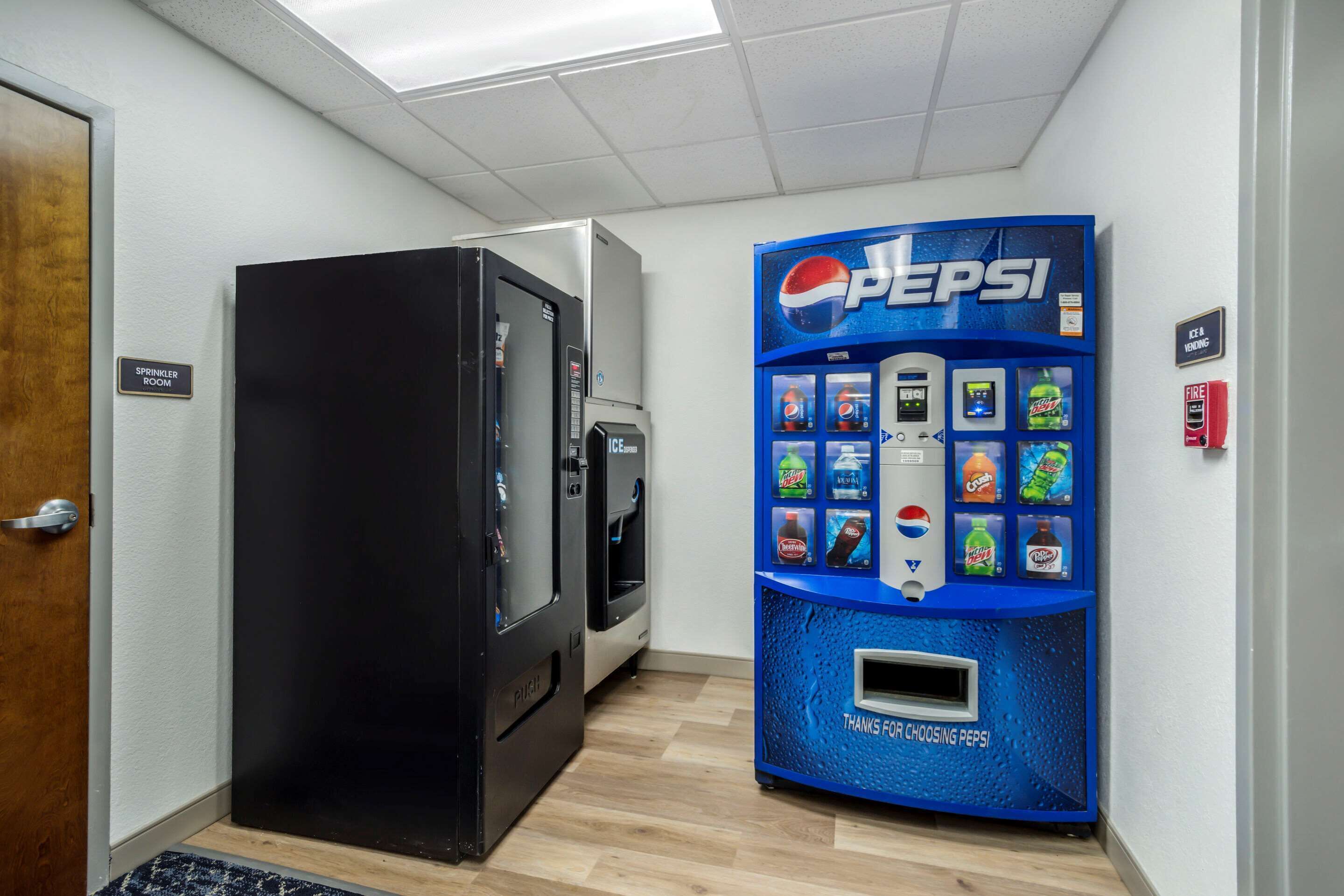 A vending machine with Pepsi options and a refrigerator in a hallway.