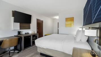 Habitación de hotel con cama, escritorio, silla y televisor montado en la pared.