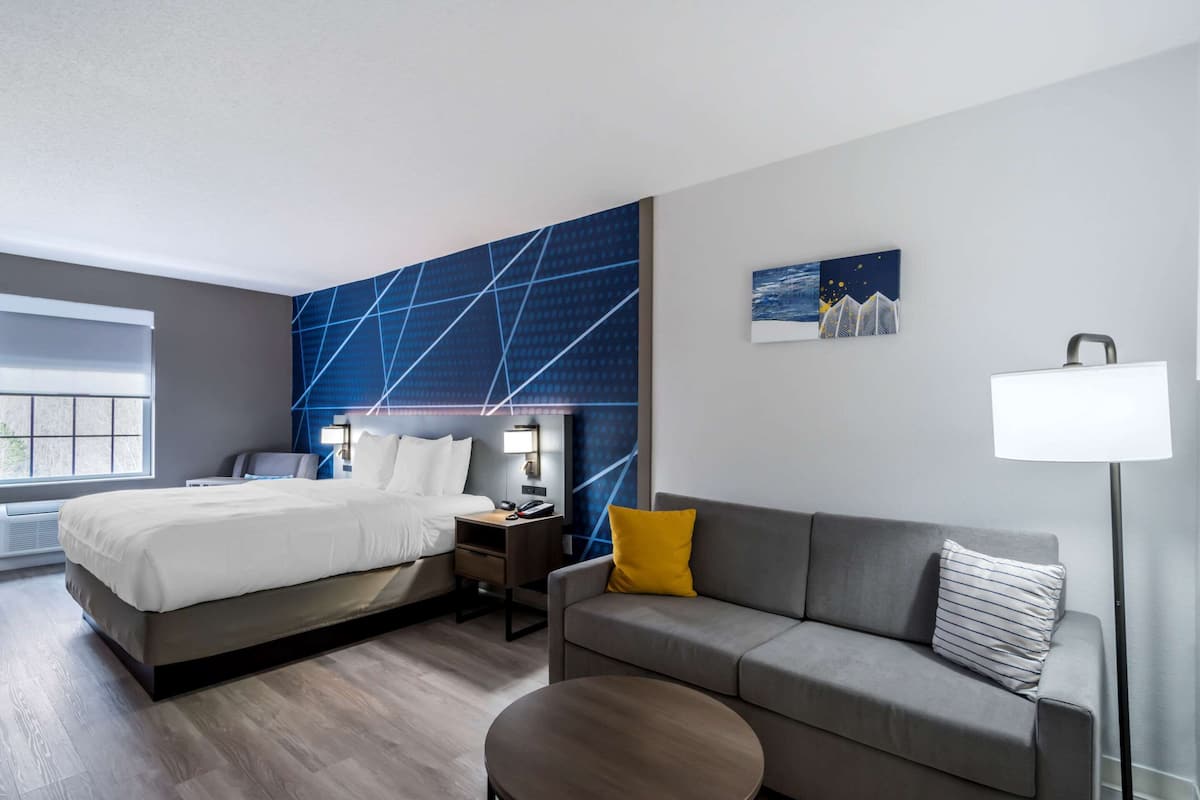 A modern hotel room with a bed, a sofa, a small table, and a nightstand.