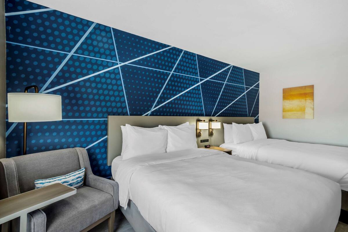A hotel room with a large bed, two bedside tables, a chair, and a wall with a geometric pattern.