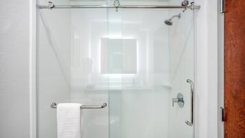 A glass-enclosed shower with a white towel on the door handle, a glass door, and a wooden door frame.
