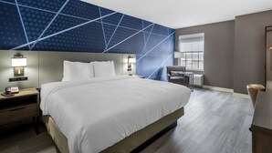 Een hotelkamer met een groot bed, nachtkastjes met lampen, een bureau en een raam met uitzicht.