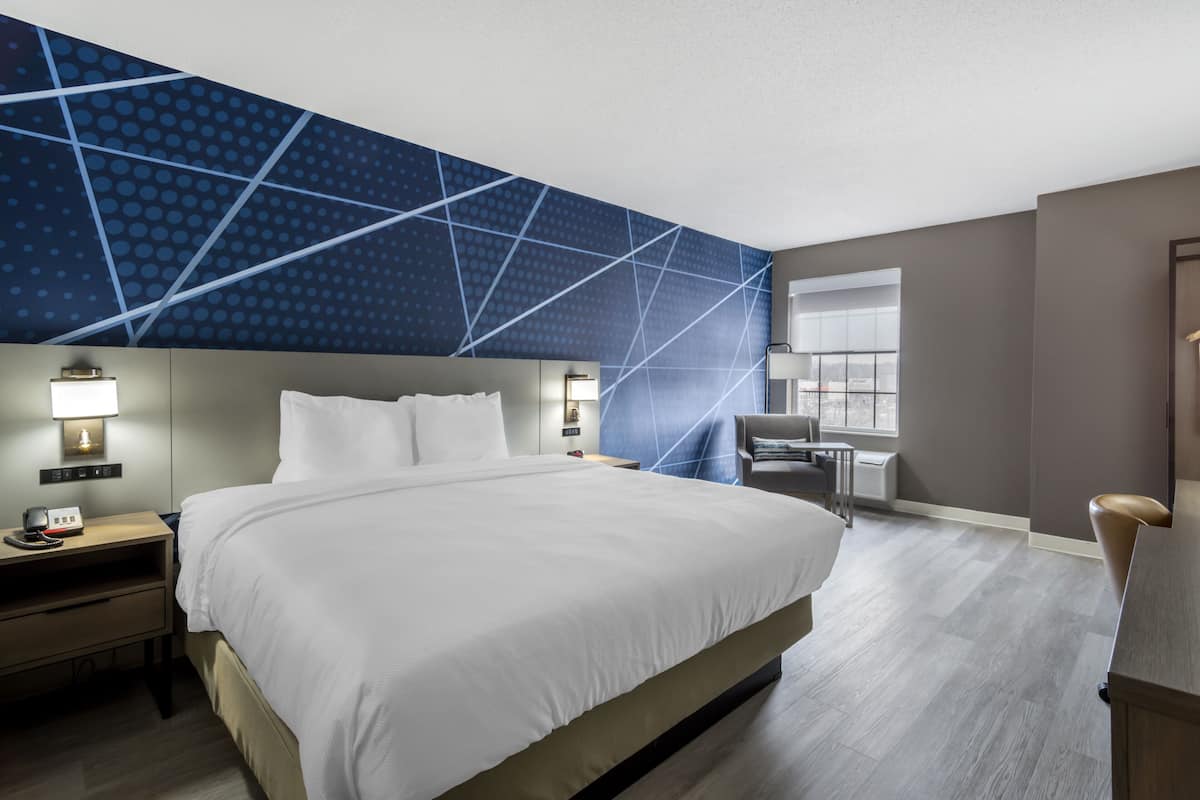 A hotel room with a large bed, bedside tables with lamps, a desk, and a window with a view.