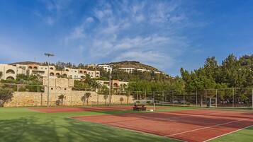 Una cancha de tenis con un muro de piedra y un edificio con arcos al fondo.
