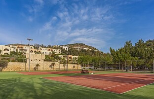 Una cancha de tenis con un muro de piedra y un edificio con arcos al fondo.