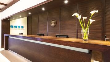 A reception desk with a wooden finish, a glass vase with white flowers, and a wall clock.